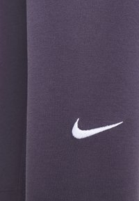 Nike Sportstoff in tiefem Lila, mit glatter Textur und weißem gesticktem Logo. Nahaufnahme der Strickdetails des Materials.