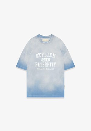 T-shirt tie-dye bleu clair, manches courtes, avec un texte blanc : "ATELIER 2018 RETERNITY DIRECTEUR CRÉATIF." Matière en coton, coupe décontractée.