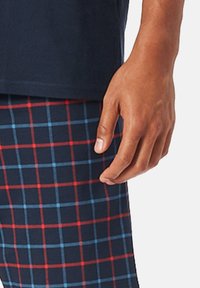Camică cu mânecă scurtă bleumarin, asociată cu pantaloni de pijama bleumarin cu un model în carouri, având o plasă de pătrate roșii și albastre deschise. Textură de material moale.