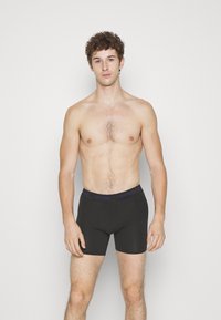 Zwarte boxershorts van rekbaar materiaal, met een grijze tailleband waarop in paarse tekst het "Calvin Klein" logo is afgebeeld.