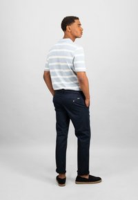 Chemise à manches courtes avec des rayures bleu clair et blanches, associée à un pantalon marine foncé et des chaussures noires à enfiler, vue de dos.