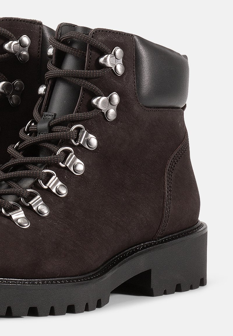 Donkerbruine suède laarzen met een rubberen zool, metalen details en grijze veters. Voorzien van een gewatteerde zwarte kraag en getextureerde accenten.