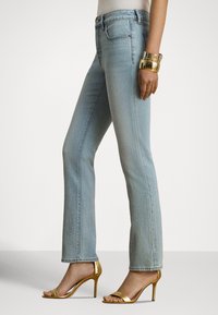 Gaiši zili džinsa džinsi ar taisnu kāju griezumu un nelielu atplērumu apakšā, kombinēti ar metāliskas zelta krāsas augstpapēžu sandaletēm.