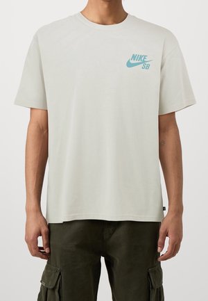 T-shirt en coton gris clair à manches courtes, col rond, avec un petit logo Nike SB turquoise sur le côté gauche de la poitrine.