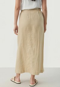 Beige linne maxikjol med elastisk midja, med rak skärning och slät textur. Enfärgad design som når till mitt på vaderna, kombinerad med sandaler.