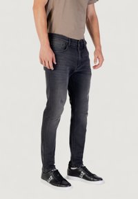 Jeans en denim noir ajustés avec un léger effet usé, design à cinq poches et texture lisse, associés à des baskets noires.