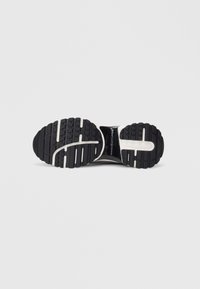 Čierna atletická podrážka so gumovým dezénom, so zvýraznenými drážkami, ryhami a bielymi akcentmi pozdĺž strednej podrážky a strán.