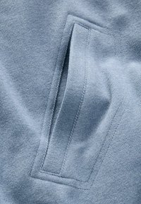 Light blue fabric with a soft, textured surface features a rectangular pocket with clean edges and visible stitching.