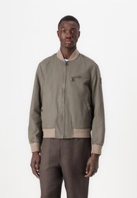 Jachetă bomber verde cu închidere cu fermoar, mansete și tiv din material elastic, buzunare laterale și un buzunar pe piept. Fabricată dintr-un material ușor.