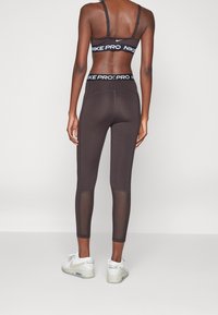 Schwarzer Nike Pro Sport-BH und passende Leggings, die ein Mesh-Panel an der Unterschenkelpartie aufweisen. Glatte Stoffe mit Logo-Akzenten und elastischen Bändern.