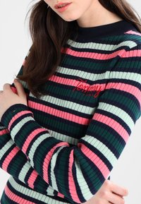 Sweter w paski o prążkowanej fakturze, z zielonymi, różowymi i granatowymi paskami. Wyhaftowane logo "Tommy" na piersi. Okrągły dekolt i długie rękawy.