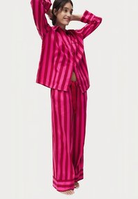 Ensemble pyjama rayé rose composé d'une chemise à boutons et d'un pantalon à jambes larges, fabriqué dans un tissu lisse avec une coupe décontractée et une taille à cordon.