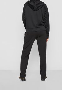 Sudadera negra con una textura suave, presenta un cuello alto y capucha. Combinada con pantalones negros, ambos tienen un ajuste relajado y cintura elástica.