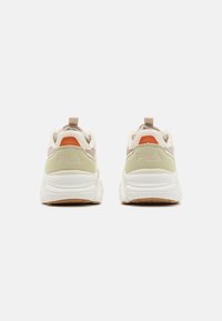 Bakside av FILA sneakers med hvit såle, lysegrønn detaljer, beige overdel og oransje detaljer. Har en pull-tab for enkel påkledning.