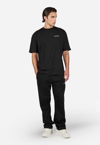 T-shirt noir à col rond et manches courtes, associé à un pantalon de jogging noir assorti. Les deux présentent un design minimaliste et des accents de logo.