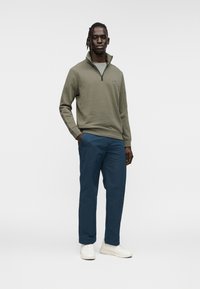 Φλις μπλούζα σε ελαιόχρωμο με ψηλό γιακά και σκούρο μπλε φαρδιά παντελόνια, συνδυασμένα με λευκά αθλητικά παπούτσια. Απλός, καθαρός σχεδιασμός.