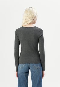Grå, ribbestrikket topp med lange ermer og rund hals. Brukes sammen med lys blå high-waisted jeans med detaljer i bakre lomme.