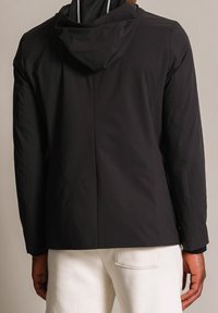 Czarna wodoodporna kurtka z kapturem, gładką fakturą, elastycznymi mankietami i detalem wentylacyjnym z tyłu. Posiada minimalistyczny design i praktyczne kieszenie.