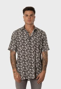 Camisa de manga corta en blanco y negro con un patrón de flores y calaveras, con cuello y cierre de botones en la parte frontal. Fabricada con tejido ligero.