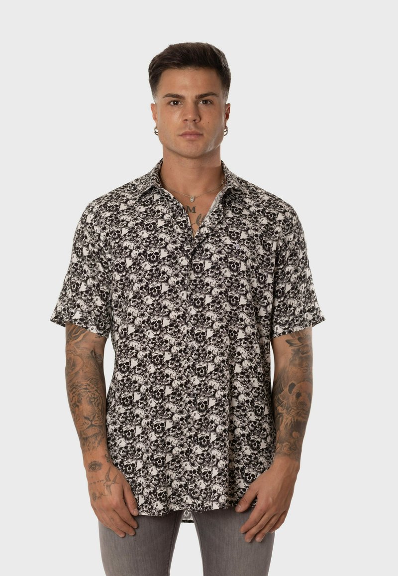 Camisa de manga corta en blanco y negro con un patrón de flores y calaveras, con cuello y cierre de botones en la parte frontal. Fabricada con tejido ligero.