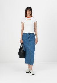 White cotton t-shirt with orange neckline and "calvin klein" text, paired with a blue denim midi skirt. Black handbag and white slip-on shoes.