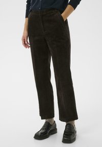 Pantalon en velours côtelé marron avec une coupe droite, texture côtelée, poches frontales et une taille confortable, associé à des mocassins noirs.