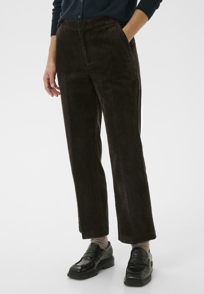 Pantalon en velours côtelé marron avec une coupe droite, texture côtelée, poches frontales et une taille confortable, associé à des mocassins noirs.