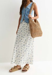 Denim vest met knopen, bloemen maxi rok in wit en blauw, tan sandalen met gespen, en een geweven bruin schoudertas.
