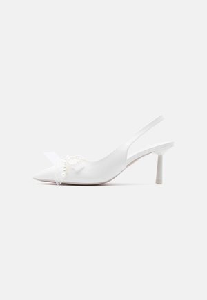 Białe szpilki typu slingback z ostrym noskiem, z delikatną kokardką zdobioną małymi perłami z przodu.