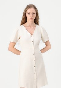 Beige linnen jurk met korte poeffmouwen, V-hals en een rij knopen aan de voorkant, met een getailleerde taille en een uitlopende rok.
