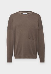 Brun langermet genser med rund hals, med en frontlomme og et strukturert strikkedesign. Passformen er avslappet og ermene er litt senket.