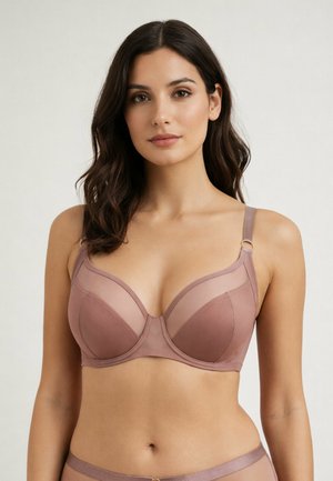 Kobieta z długimi ciemnymi włosami, ubrana w mauve stanik z fiszbinami i przezroczystymi panelami, stoi na jasnym, jednolitym tle.