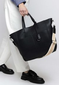 Black leather tote bag with a textured finish, featuring dual top handles and a long adjustable strap in contrasting tan.