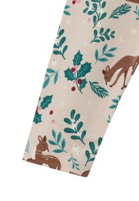 Leggingstof met een beige achtergrond waarop groene hulstbladeren, rode bessen en bruine herten in verschillende poses zijn afgebeeld.