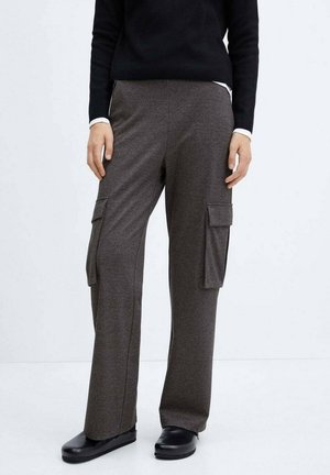 Person trägt dunkelgraue, weite Cargo-Hosen mit Klappentaschen, schwarze Slip-On-Schuhe und ein schwarzes Langarmshirt mit weißen Manschetten.