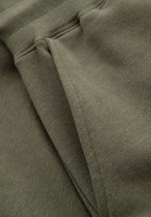 Gros plan sur un tissu vert kaki montrant des coutures et un matériau plié avec un détail de ceinture côtelée.