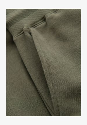 Gros plan sur un tissu vert kaki montrant des coutures et un matériau plié avec un détail de ceinture côtelée.