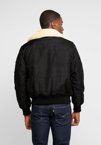 Chaqueta bomber negra con un cuello de piel sintética, puños acanalados y cinturilla. El material tiene una textura suave y un diseño ajustado.