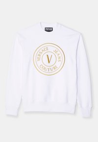 Vit sweatshirt med rund hals, med en stor guldfärgad cirkulär logotyp med texten "VERSACE JEANS COUTURE" och en upphöjd central "V"-emblem.
