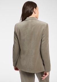 Blazer in velluto verde oliva con design monopetto, rever a incavo e trama liscia, caratterizzato da una vestibilità su misura e cuciture posteriori.