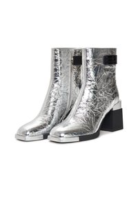 Metallisch silberne Stiefeletten mit strukturiertem Finish, seitlichem Reißverschluss und Blockabsatz. Akzentuiert mit einem schwarzen Etikett an der oberen Seite.
