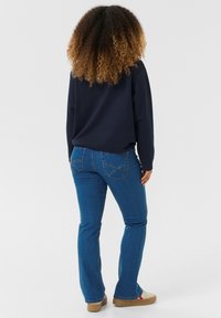 Modré džíny z denimu s rozšířeným designem nohavic, spárované s námořnickou košilí s dlouhým rukávem. Viditelné švy a volnočasové hnědé boty.