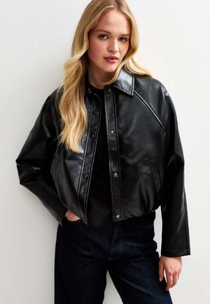 Zwart leren cropped jack met drukknoopjes, puntige kraag en zijzakken, gecombineerd met donkerdenim jeans. Gladde textuur en een getailleerde pasvorm.