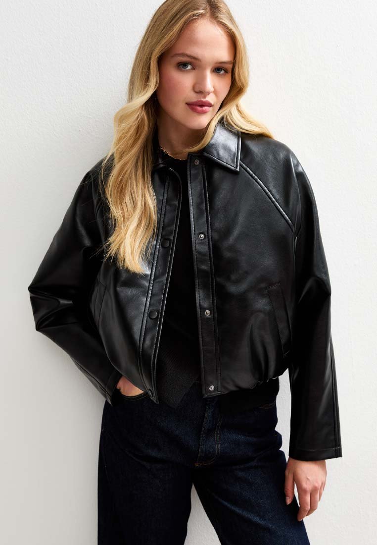 Veste cropped en cuir noir avec boutons-pression, col pointu et poches latérales, associée à un jean en denim foncé. Texture lisse et coupe ajustée.