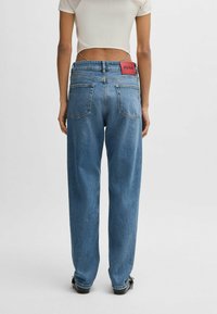 Blå högmidjade jeans med avslappnad passform, med en röd logotypapplikation på baksidan, två bakfickor och en blekt denimtextur.