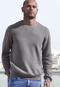 Grauer strukturierter Pullover mit einem gerippten Rundhalsausschnitt und diagonaler Musterung, kombiniert mit blauen Jeans. Glattes Strickmaterial, lange Ärmel, lockere Passform.