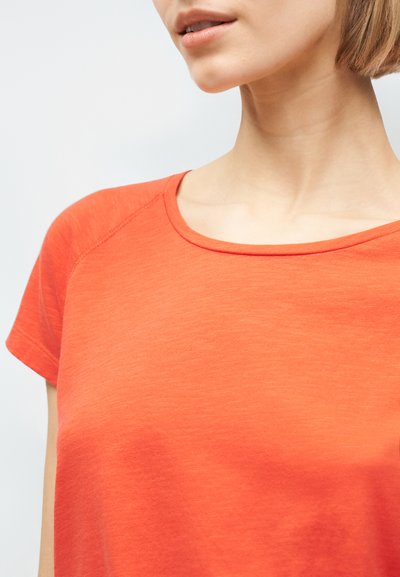 Γυναίκα που φοράει φωτεινό πορτοκαλί μπλουζάκι κοντομάνικο με στρογγυλή λαιμόκοψη και μαλακή υφή υφάσματος, εμφανίζεται από το πηγούνι έως το πάνω μέρος του στήθους.