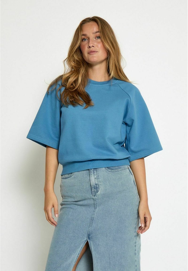 Felpa blu in cotone con maniche raglan corte, caratterizzata da una vestibilità rilassata e orlo a coste, abbinata a una gonna di jeans chiaro con spacco frontale.