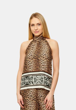 Donna con lunghi capelli biondi che indossa un top smanicato con stampa leopardata con bordo decorato in bianco e nero, abbinato a pantaloni coordinati.