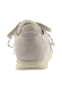 Zapatilla de ante beige con suela crema, cordones blancos y negros con patrón, vista desde el talón con el logo "victoria" en la lengüeta trasera.